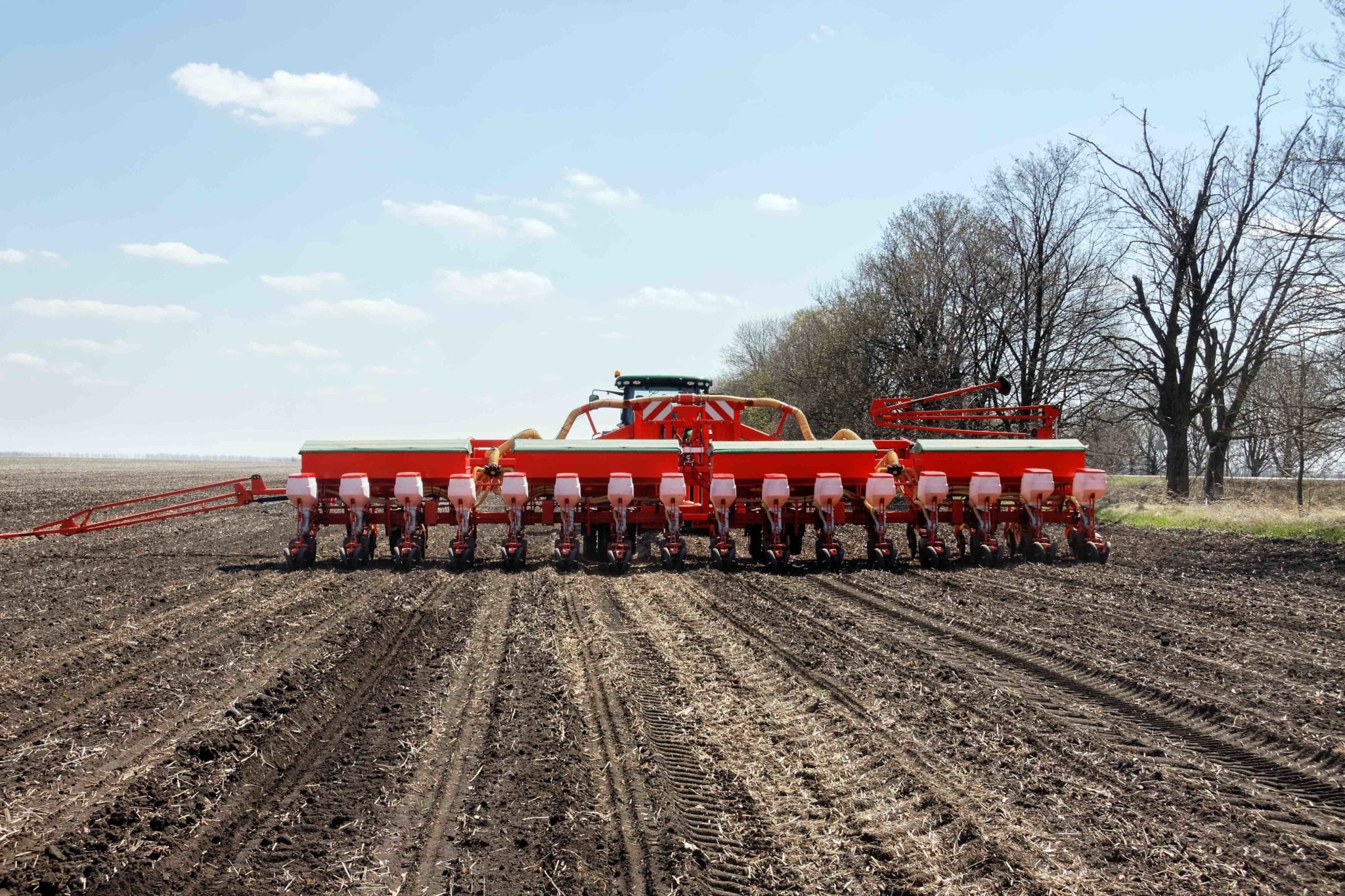 Tractor with trailed planter working in field in a sunny spring day